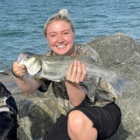 Connie with her bass catch on rocks with sea in the background