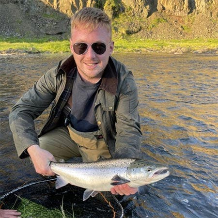 Young man with aviator glasses on holding his first sea trout catch by the river side