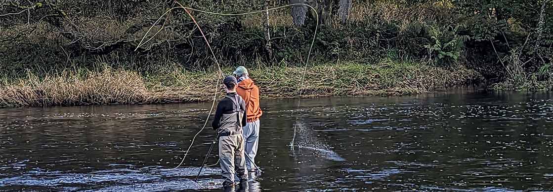 A young fly fishing guide instructs a rugby player, from Newcastle Falcons, whilst in the middle of the river