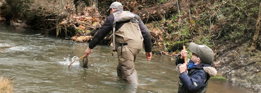 Father teaching his son to fly fish, both wading in the river